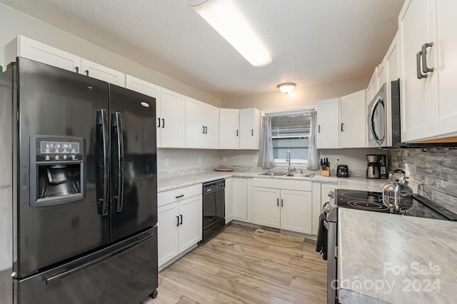 kitchen featuring a textured ceiling, sink, black appliances, light hardwood / wood-style flooring, and white cabinets