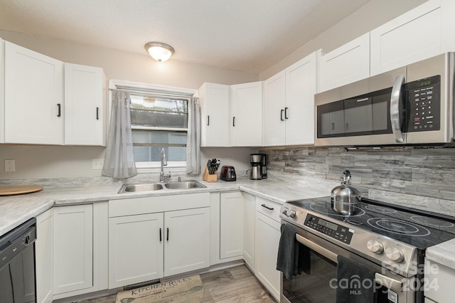 kitchen featuring decorative backsplash, appliances with stainless steel finishes, sink, light hardwood / wood-style flooring, and white cabinets