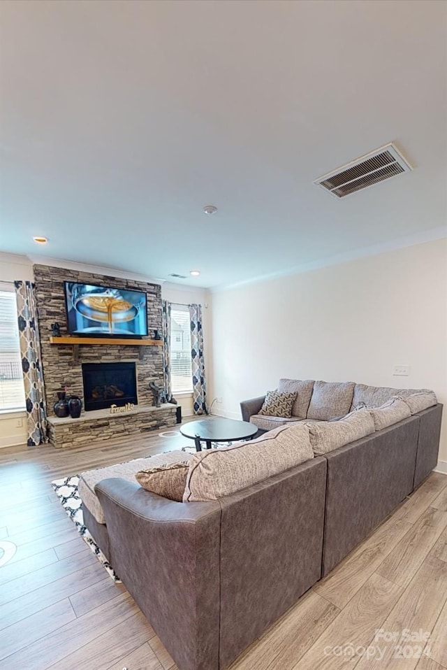 living room with a stone fireplace, a healthy amount of sunlight, and light wood-type flooring