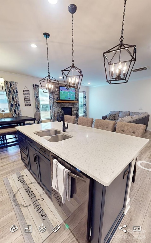 kitchen featuring sink, a kitchen island with sink, pendant lighting, and light wood-type flooring