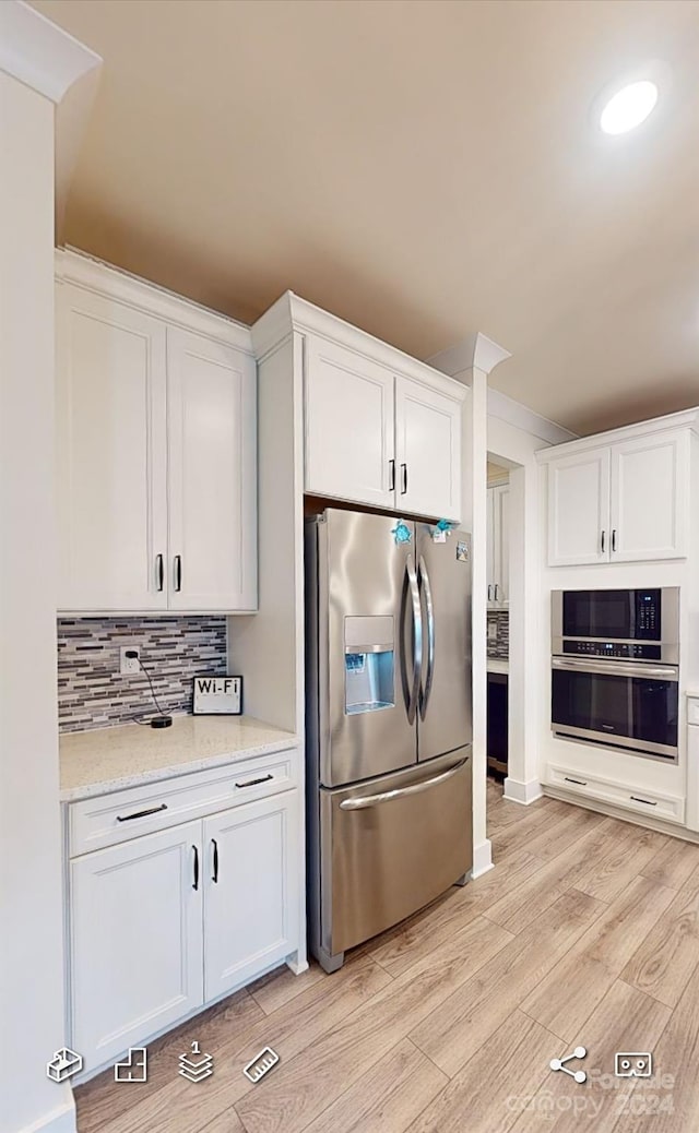 kitchen with stainless steel appliances, backsplash, light stone countertops, light wood-type flooring, and white cabinets