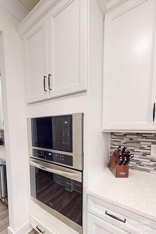 kitchen with white cabinets, backsplash, light stone countertops, hardwood / wood-style flooring, and stainless steel appliances