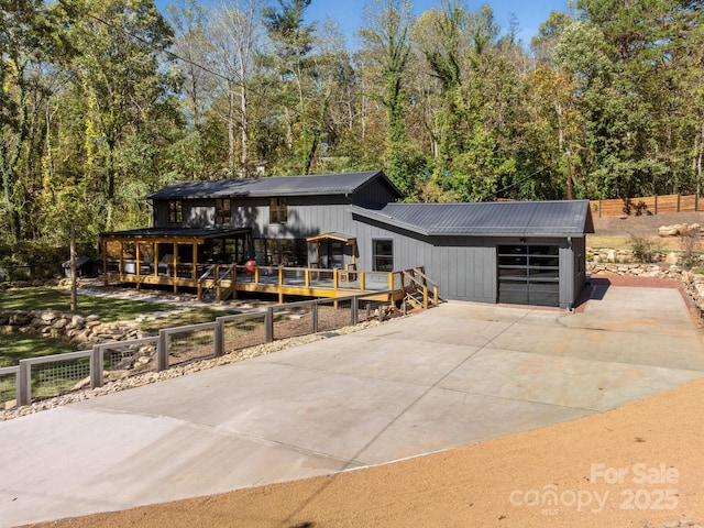 view of front of property with metal roof, a deck, fence, a garage, and driveway