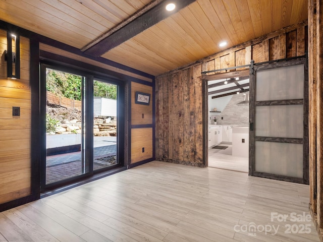 empty room with a barn door, wooden walls, wooden ceiling, beamed ceiling, and wood finished floors