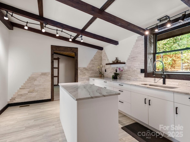 kitchen featuring a sink, white cabinetry, decorative backsplash, beam ceiling, and light stone countertops