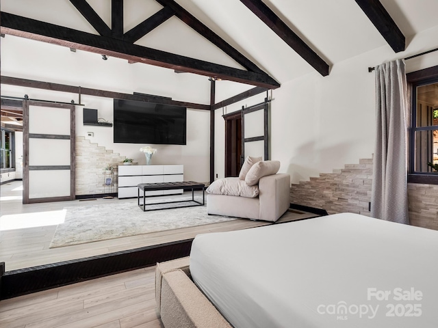 bedroom with a barn door, lofted ceiling with beams, and wood finished floors