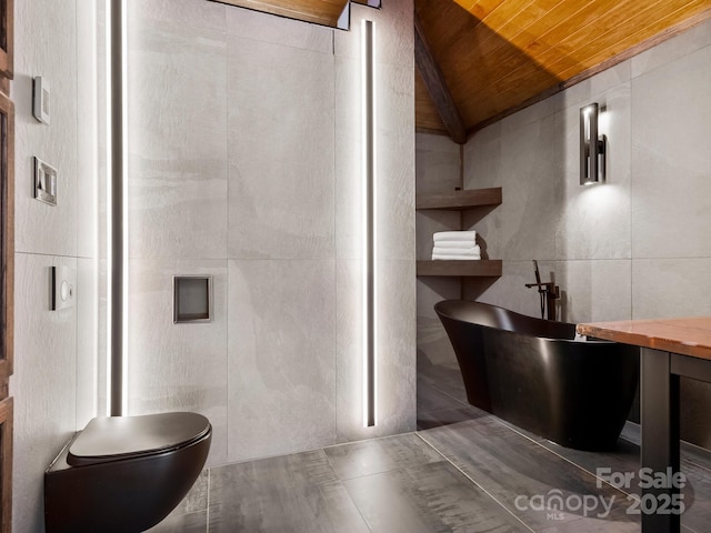 bathroom featuring tile walls, toilet, vaulted ceiling, a freestanding tub, and wooden ceiling