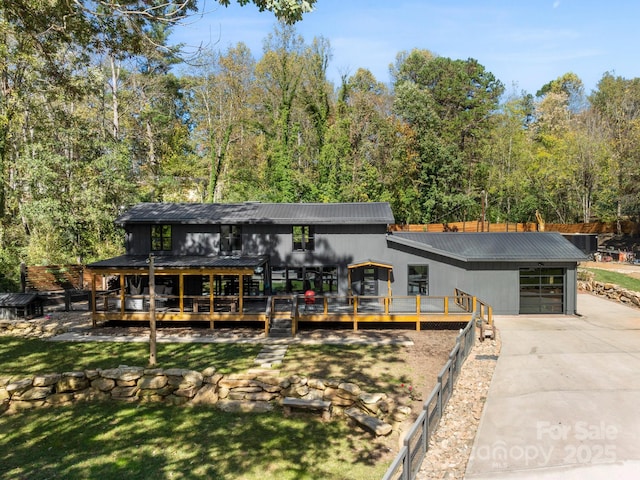 view of front of home featuring a garage, metal roof, driveway, and a forest view