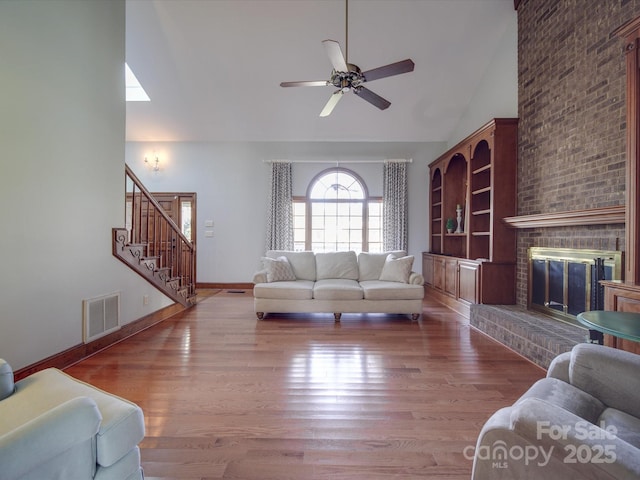 living room with hardwood / wood-style flooring, ceiling fan, a fireplace, and high vaulted ceiling