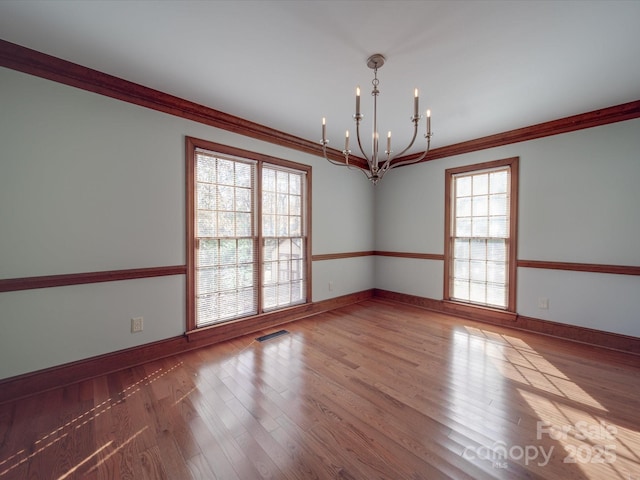 empty room featuring wood-type flooring, a notable chandelier, and crown molding