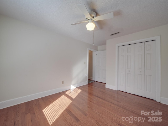 unfurnished bedroom with ceiling fan, a closet, wood-type flooring, and a textured ceiling