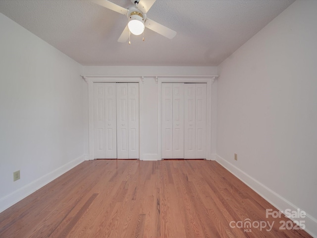 unfurnished bedroom featuring ceiling fan, two closets, a textured ceiling, and light wood-type flooring