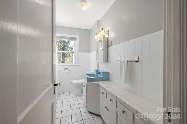 bathroom with toilet, vanity, tile walls, and tile patterned flooring