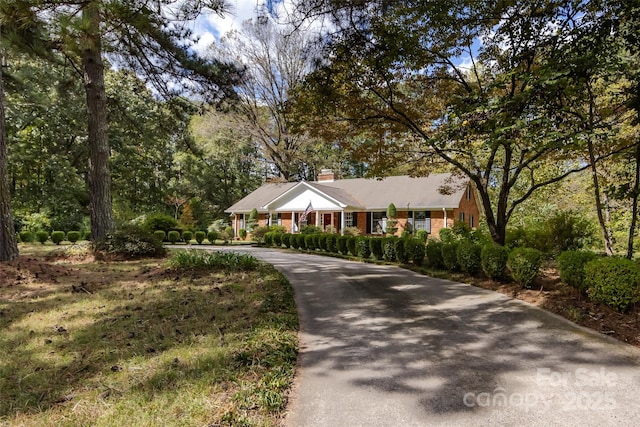 single story home featuring a chimney, concrete driveway, and brick siding