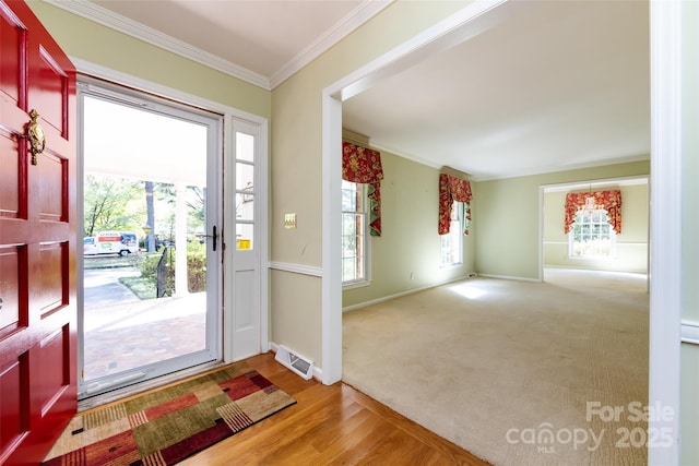 entryway featuring carpet floors, crown molding, visible vents, wood finished floors, and baseboards