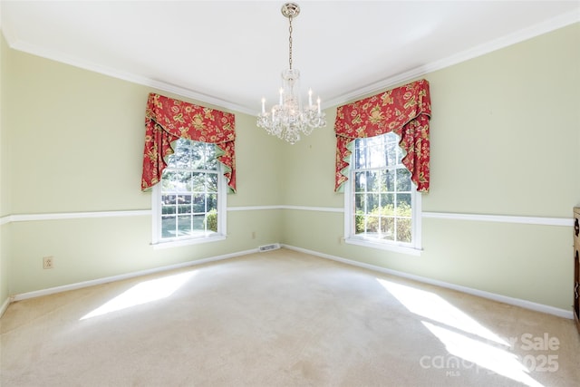 carpeted spare room with ornamental molding, visible vents, baseboards, and an inviting chandelier