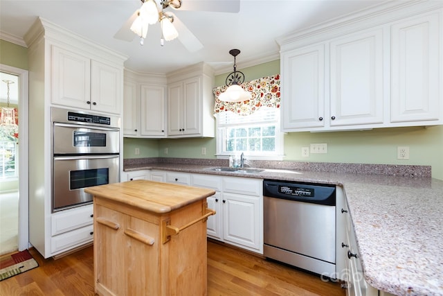 kitchen with decorative light fixtures, light wood-style flooring, appliances with stainless steel finishes, white cabinets, and a sink