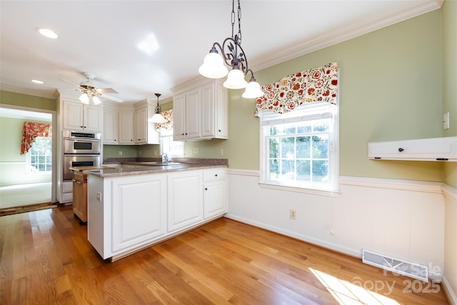 kitchen featuring pendant lighting, visible vents, double oven, white cabinets, and a peninsula