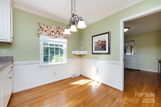 unfurnished dining area featuring ornamental molding, wainscoting, visible vents, and light wood finished floors