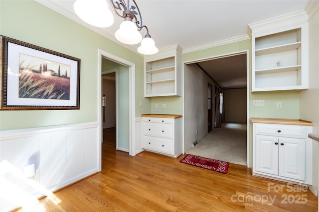 unfurnished dining area with light wood-type flooring, a wainscoted wall, and crown molding