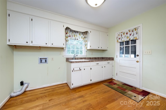 interior space featuring washer hookup, cabinet space, light wood-style flooring, a sink, and baseboards