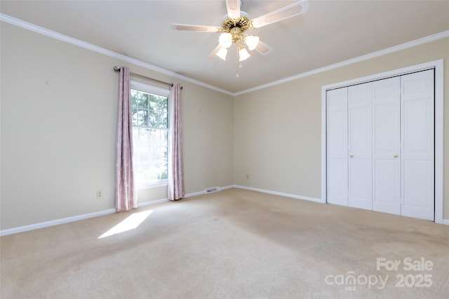 unfurnished bedroom featuring a closet, carpet flooring, crown molding, and baseboards