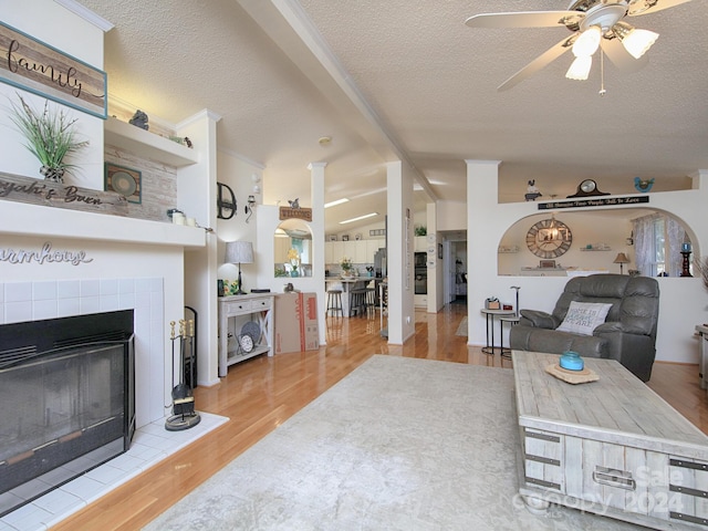 living room featuring ceiling fan, a fireplace, light hardwood / wood-style flooring, vaulted ceiling with beams, and a textured ceiling