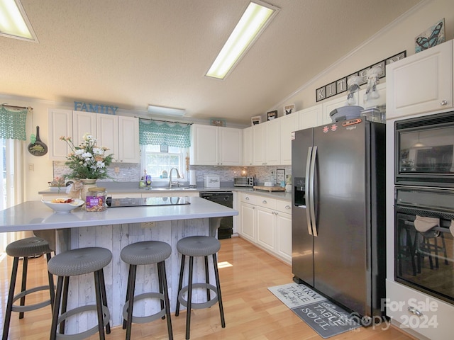 kitchen with light hardwood / wood-style flooring, lofted ceiling, black appliances, a center island, and white cabinetry