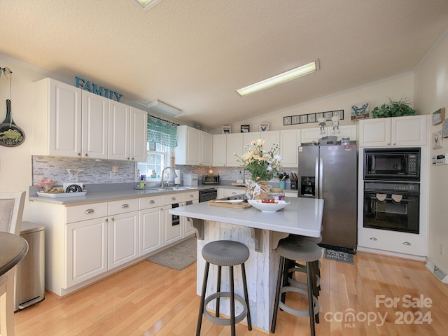 kitchen featuring light wood-type flooring, black appliances, a kitchen island, sink, and white cabinetry