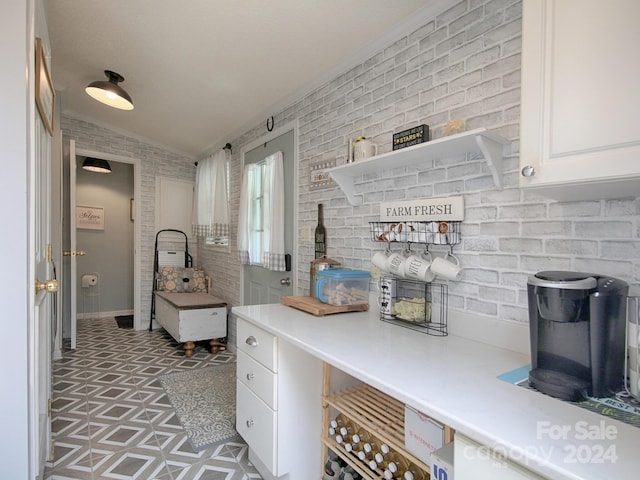 mudroom featuring dark tile patterned flooring, vaulted ceiling, and brick wall