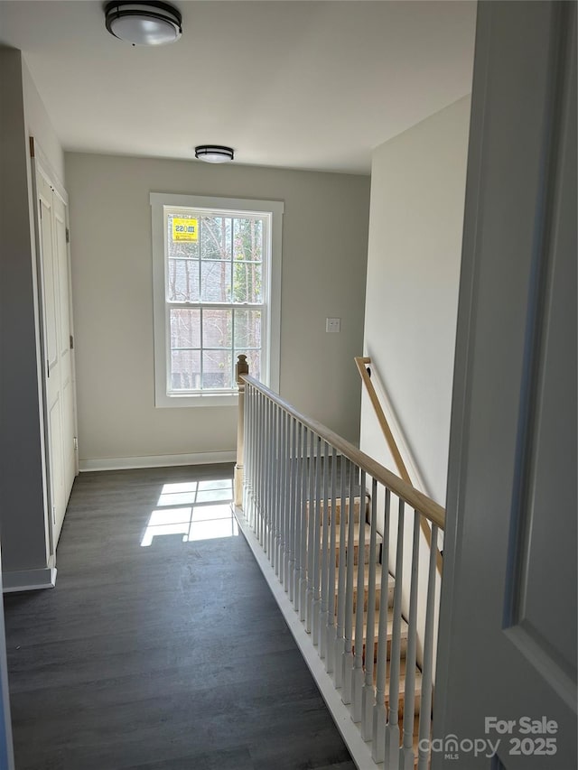 corridor featuring an upstairs landing, baseboards, and dark wood-style flooring