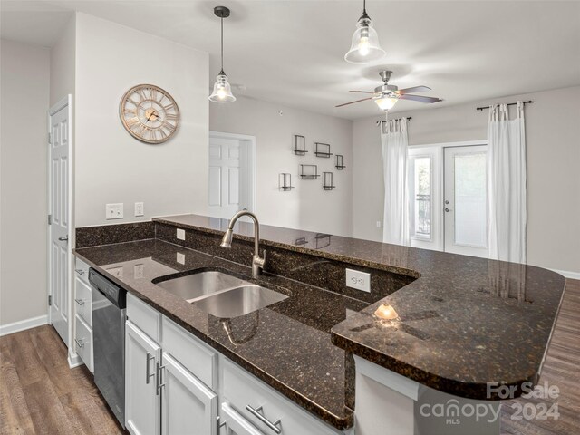 kitchen with hanging light fixtures, sink, dark wood-type flooring, dishwasher, and dark stone counters