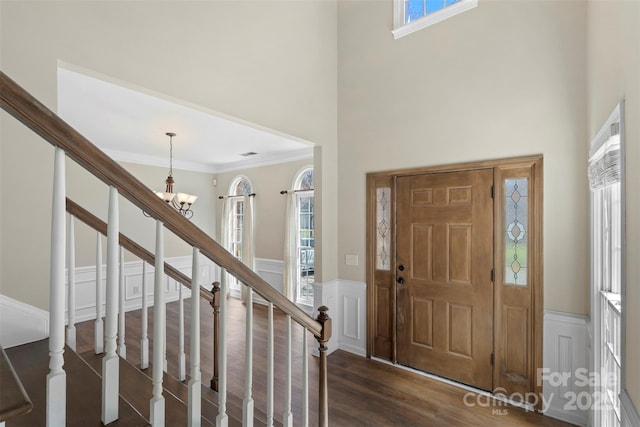 foyer featuring dark wood finished floors, a decorative wall, a high ceiling, ornamental molding, and wainscoting