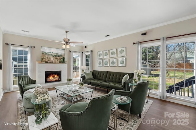 living area featuring ornamental molding, a brick fireplace, visible vents, and wood finished floors