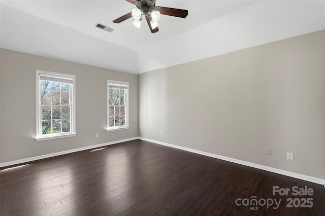 unfurnished room with vaulted ceiling, visible vents, dark wood finished floors, and baseboards