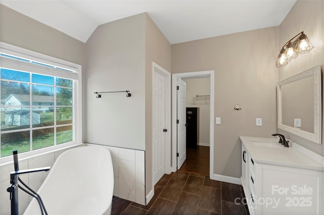 full bath with wood finish floors, vanity, a freestanding bath, vaulted ceiling, and a walk in closet