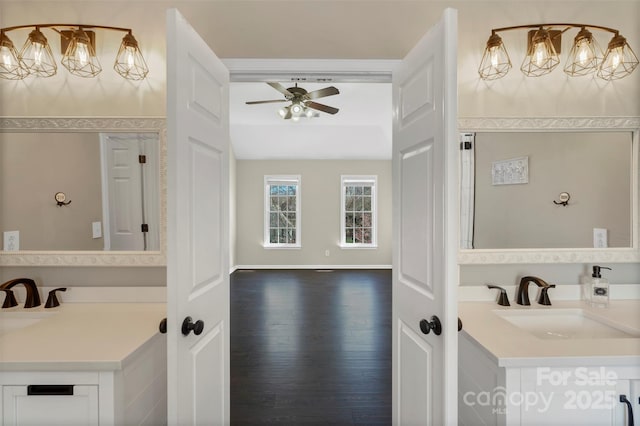 bathroom with baseboards, lofted ceiling, wood finished floors, vanity, and ceiling fan with notable chandelier