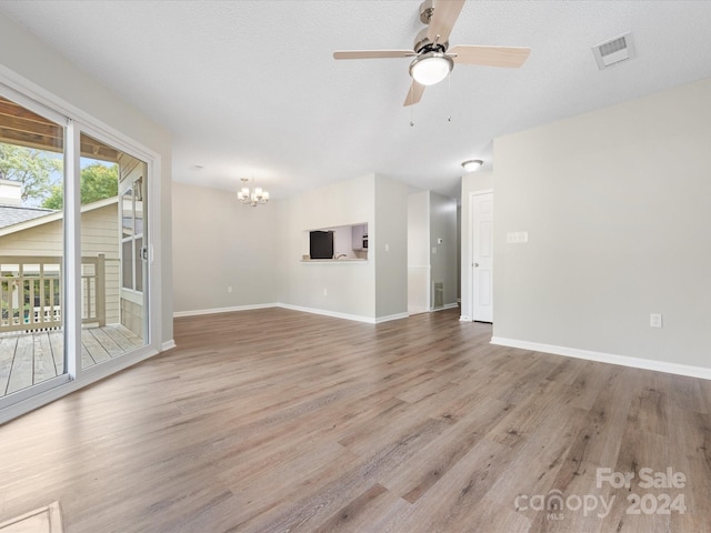 unfurnished living room featuring ceiling fan with notable chandelier, light hardwood / wood-style flooring, and a textured ceiling