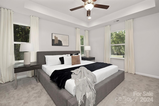 carpeted bedroom with ceiling fan and a raised ceiling