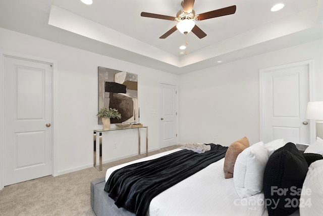 carpeted bedroom with ceiling fan and a raised ceiling