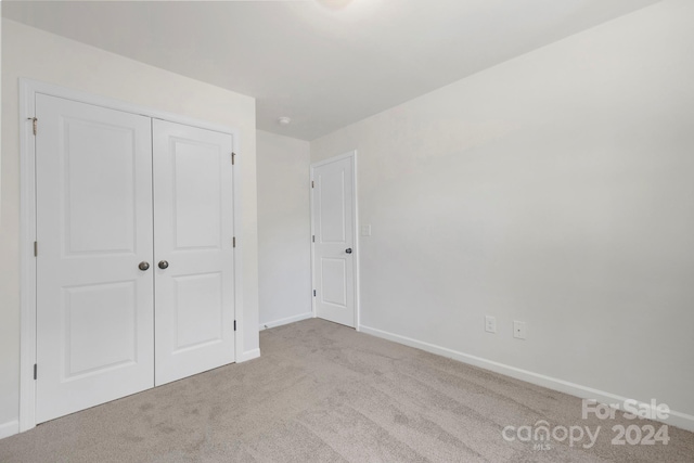 unfurnished bedroom with light colored carpet and a closet