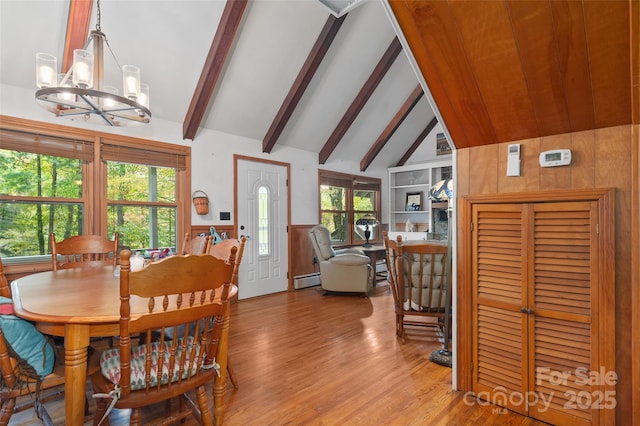 dining space with wood walls, a chandelier, lofted ceiling with beams, baseboard heating, and light hardwood / wood-style floors