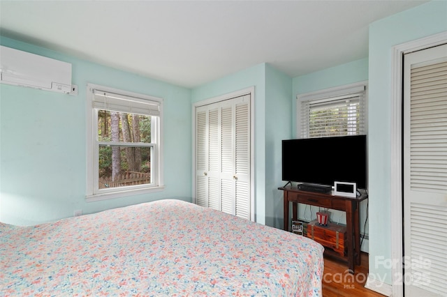 bedroom featuring a wall mounted air conditioner, wood-type flooring, and multiple closets