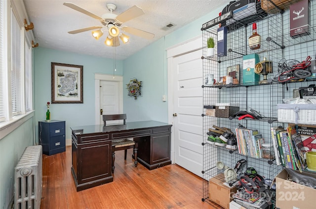 home office featuring light hardwood / wood-style floors, a textured ceiling, radiator heating unit, and ceiling fan