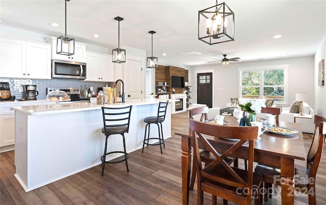 kitchen featuring appliances with stainless steel finishes, white cabinetry, a center island with sink, and dark wood-type flooring