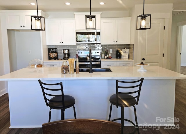 kitchen with an island with sink, stainless steel appliances, pendant lighting, and dark hardwood / wood-style flooring