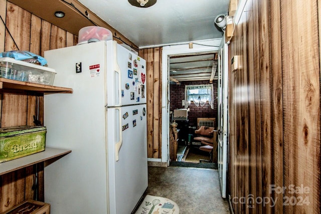 kitchen featuring concrete floors, wood walls, and white refrigerator