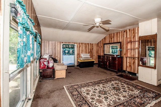 interior space featuring ceiling fan, wood walls, vaulted ceiling, and dark colored carpet