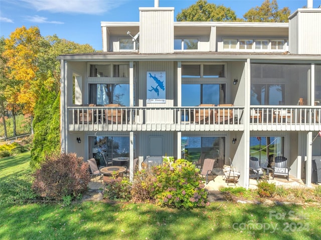 rear view of house with a balcony, a yard, and a patio