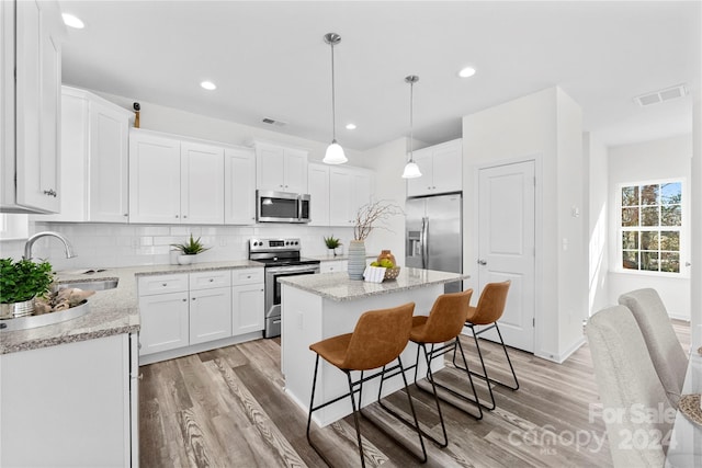 kitchen featuring light hardwood / wood-style floors, a kitchen island, decorative light fixtures, white cabinets, and appliances with stainless steel finishes